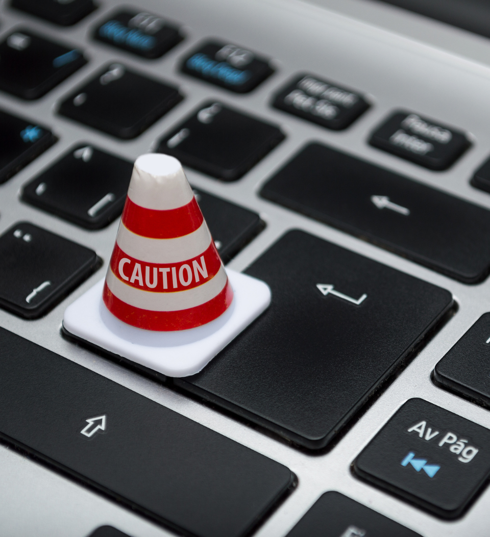 Ein kleiner orange-weißer Warnkegel sitzt in diesem Stock-Bild auf der Eingabetaste einer Computertastatur und symbolisiert eine Warnung oder einen Alarm im Zusammenhang mit der Computernutzung oder der Online-Sicherheit.